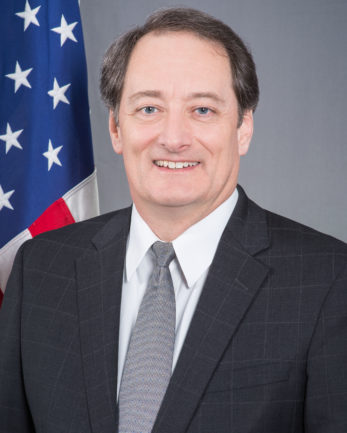 Lee McClenny, embajador de los Estados Unidos, con la bandera estadounidense.