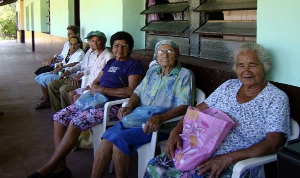 Grupo de adultos mayores sentados en un banco de un hogar.