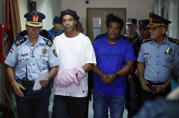 Ronaldinho y su hermano saliendo de la fiscalía, acompañados de policías.