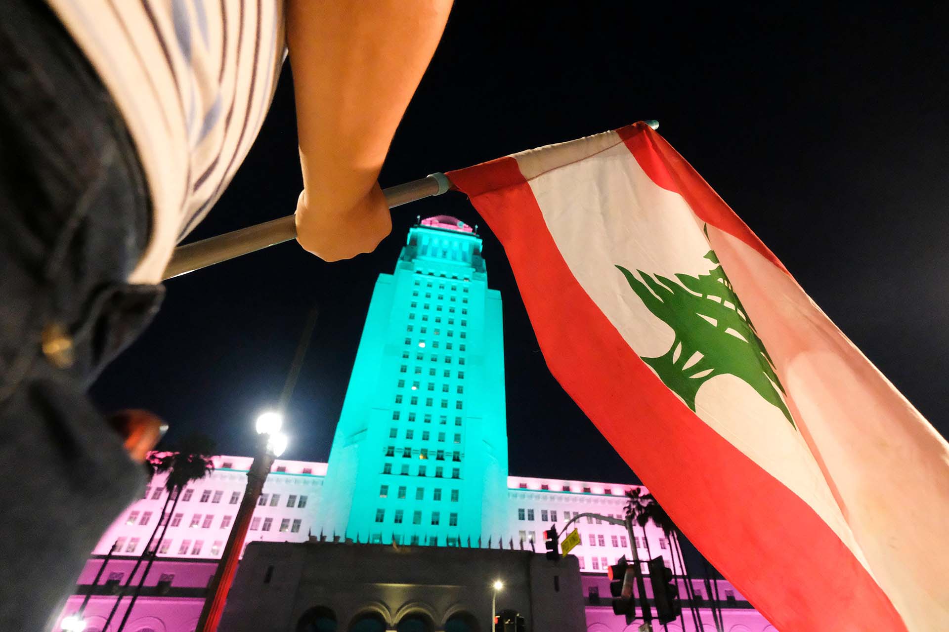 Edificio de la Municipalidad de Los Ángeles, California, iluminado con los colores de El Líbano, y una persona atajando la misma bandera.