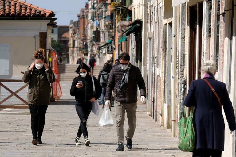 Personas recorriendo pueblo de Italia, usando mascarillas.