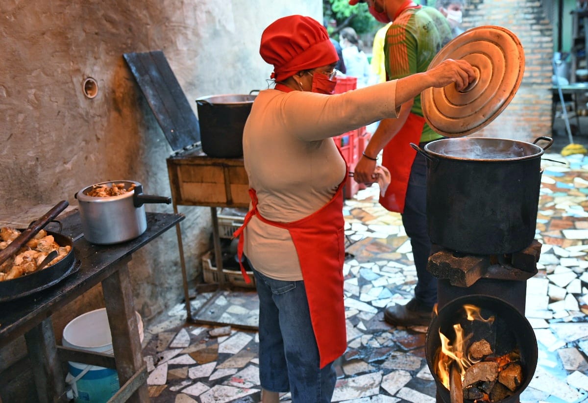 Mujer cocinando en una olla popular a la leña.
