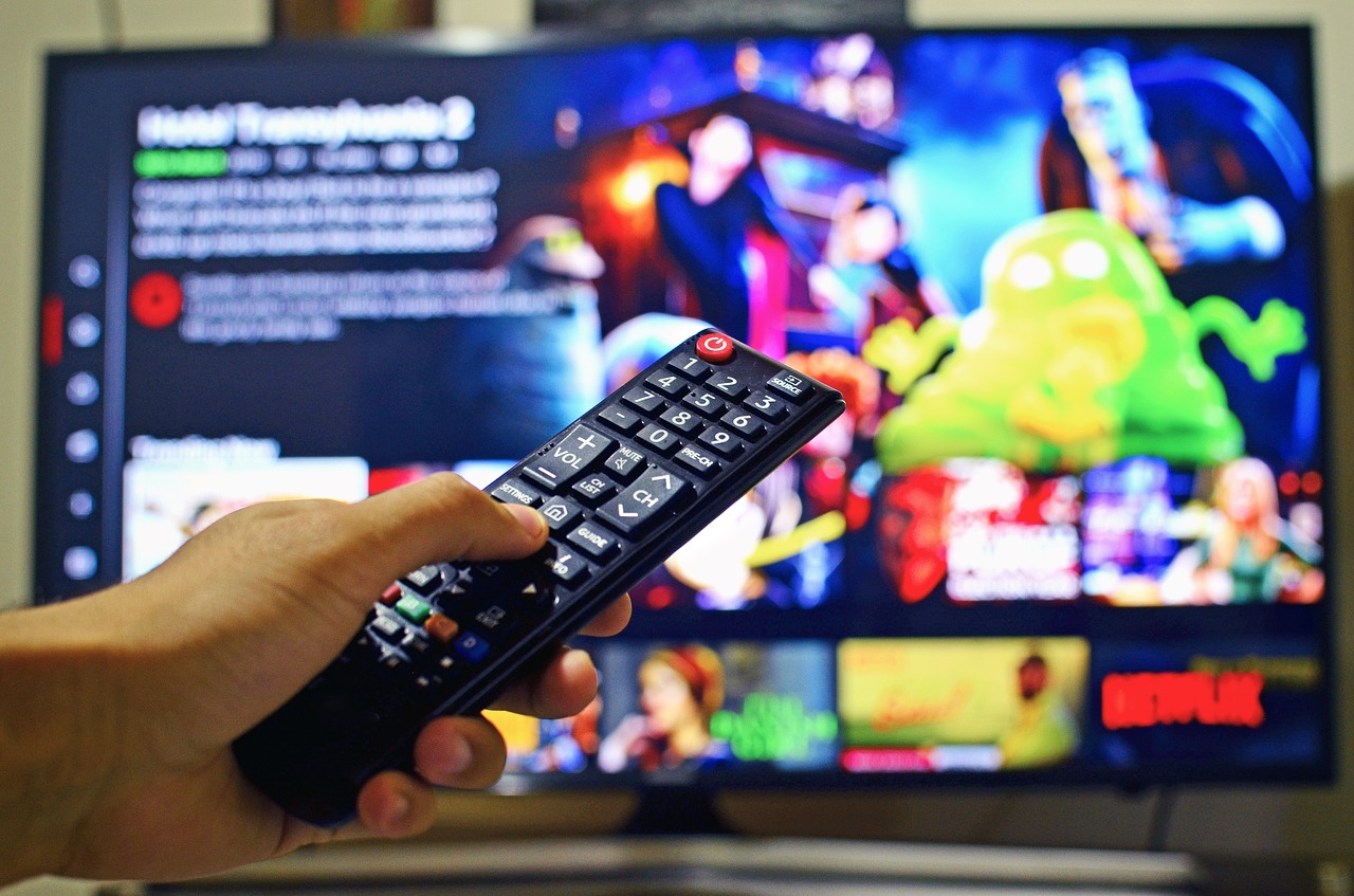 Imagen ilustrativa. Mano de una persona sosteniendo un control de Smart TV con netflix de fondo.
